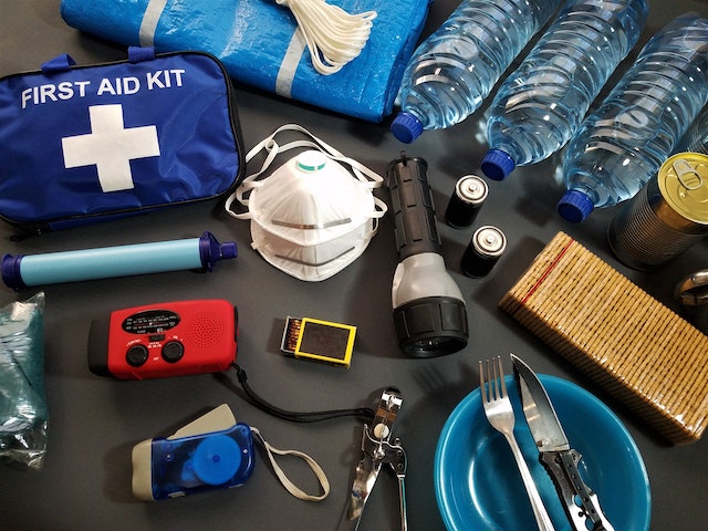a collection of emergency supplies including matches a first aid kit and bottled water are laid out on a table