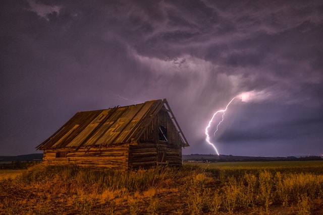a decaying farmhouse on the Saskatchewan prairies against the backdrop of a thunderstorm with purple clouds and a brilliant strike of lightning hitting the ground several kilometres away