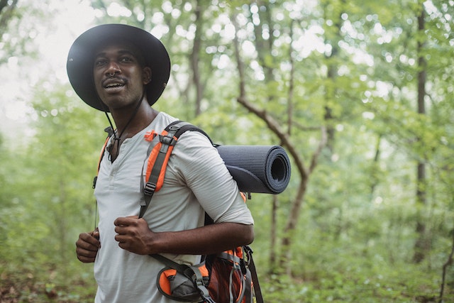 a hiker in a tee shirt and fishing hat pauses on a hiking trail to take in the scenery