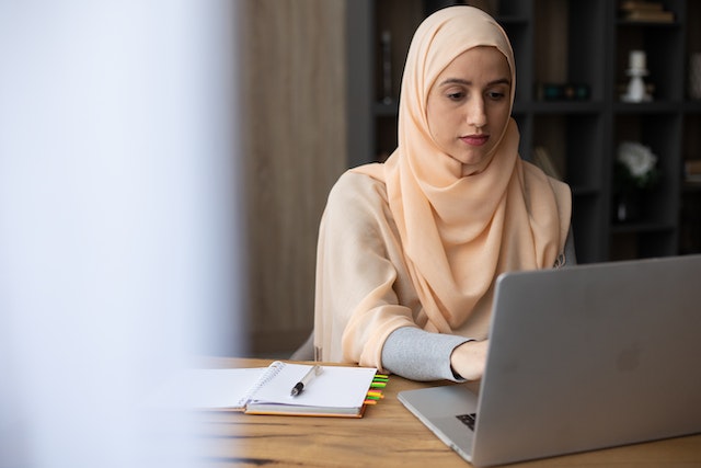 A landlord in a peach hijab sits at a desk and researches investing partners