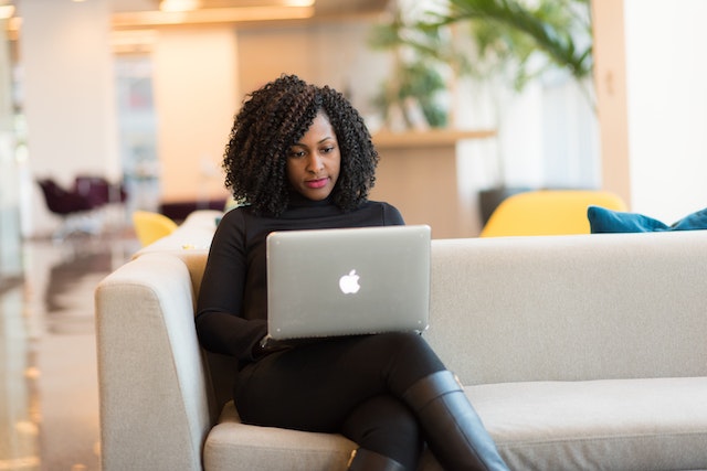 a landlord with tight natural curls sits on a white couch while emailing their tenant important documents