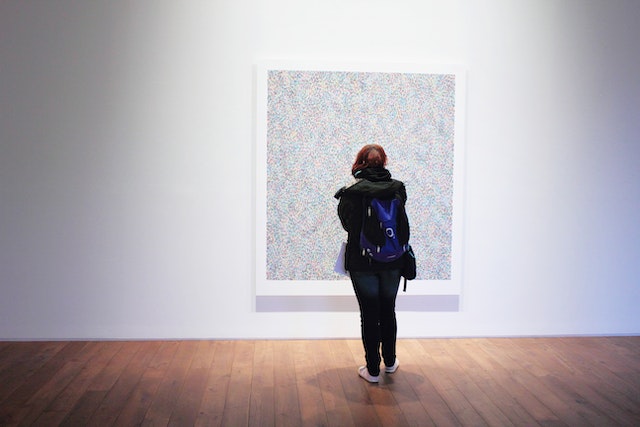 a modern art gallery patron standing in front of a canvas featuring numerous multicoloured dots