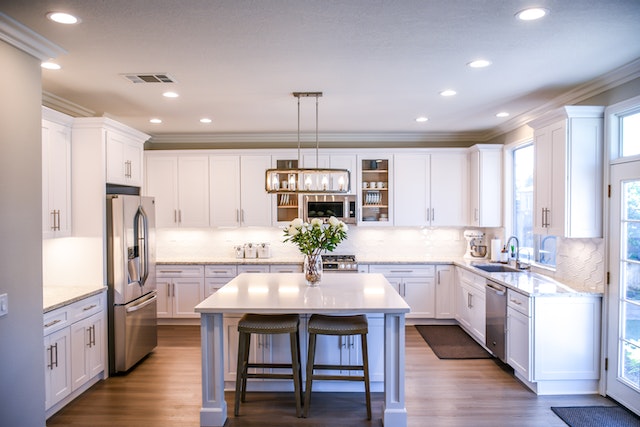 A modern kitchen with stainless steel appliances a large centre island and white marble countertops