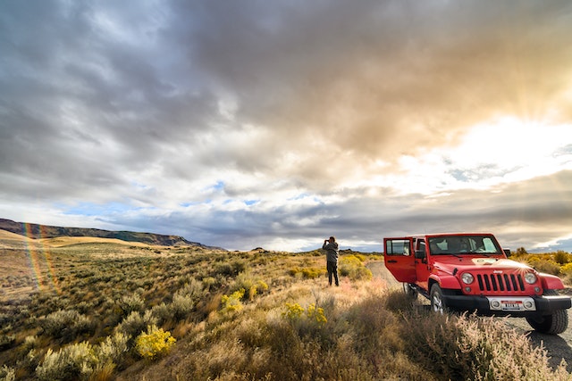 a traveller stands near their red jeep and takes a picture of a scenic valley in central saskatchewan