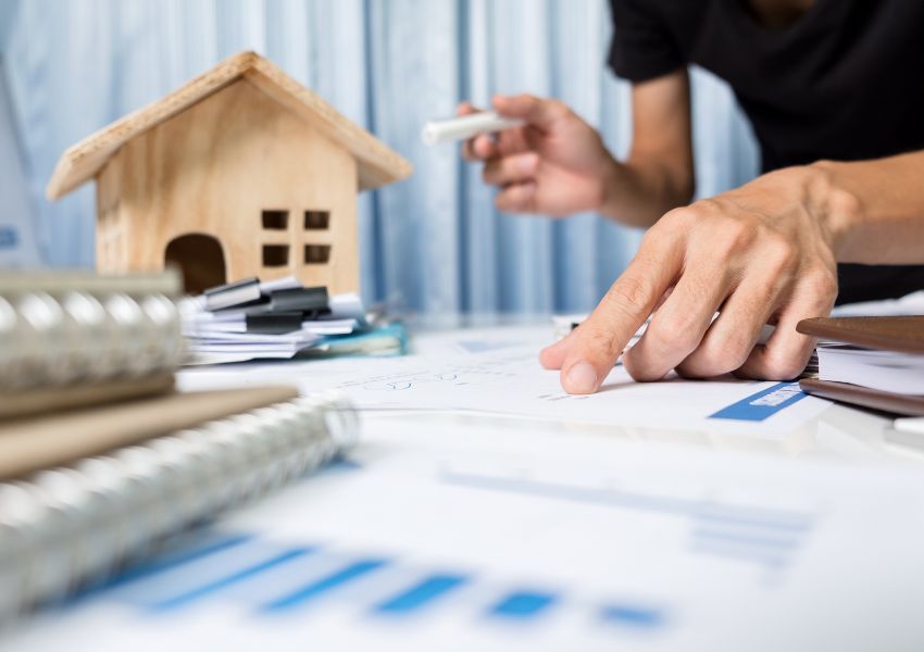 person looking over stats and graphs with a wooden house figurine in the background