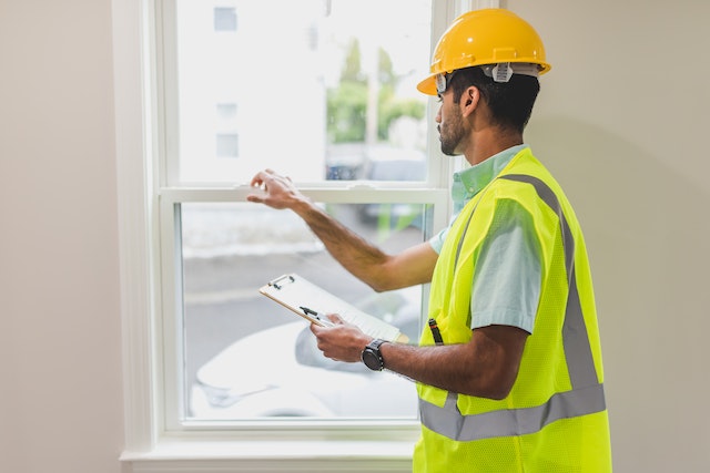 a home inspector in a hardhat and yellow vest inspects a window
